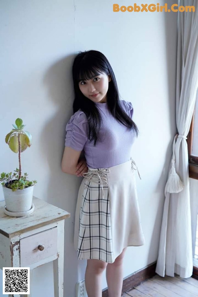 A woman standing in front of a window wearing a skirt.