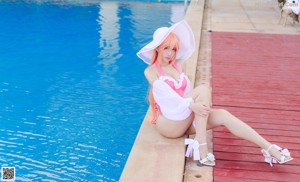 A woman in a pink bathing suit and a white hat by a pool.