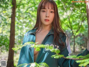A woman in a green sweatshirt and white thong is standing in the woods.