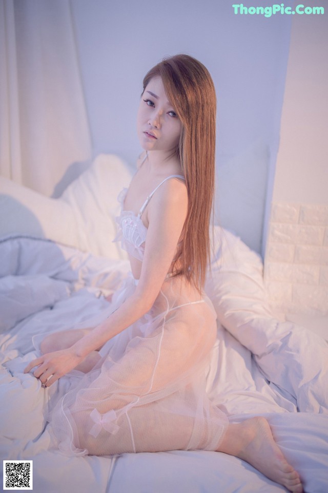 A woman sitting on a bed in a white lingerie.