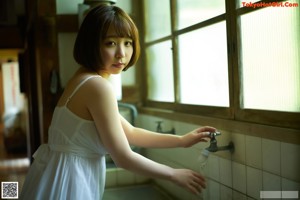 A naked asian woman holding a blue bra in her hand.
