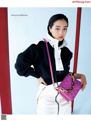 A woman in a black sweater and white pants holding a purple purse.