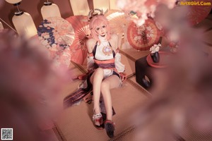 A woman with pink hair is posing naked on a bed.