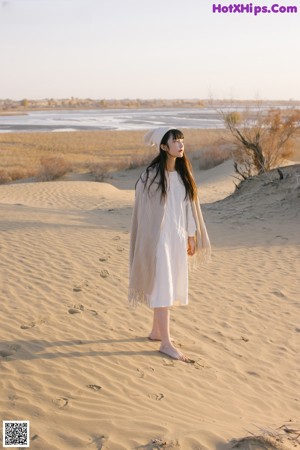 A woman sitting on top of a sand dune in the desert.