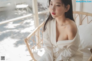 A woman sitting on a wicker chair with a pillow.
