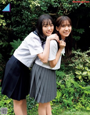 Two young women standing next to each other in front of a tree.