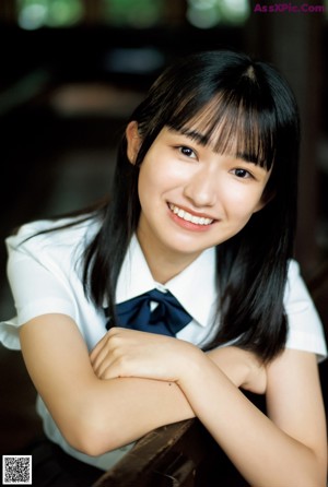 A young woman sitting on a wooden bench in a school uniform.