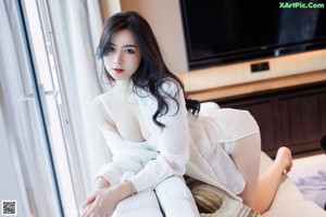 A woman sitting on a couch in a white shirt.
