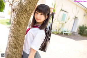 A woman in a school uniform leaning against a tree.