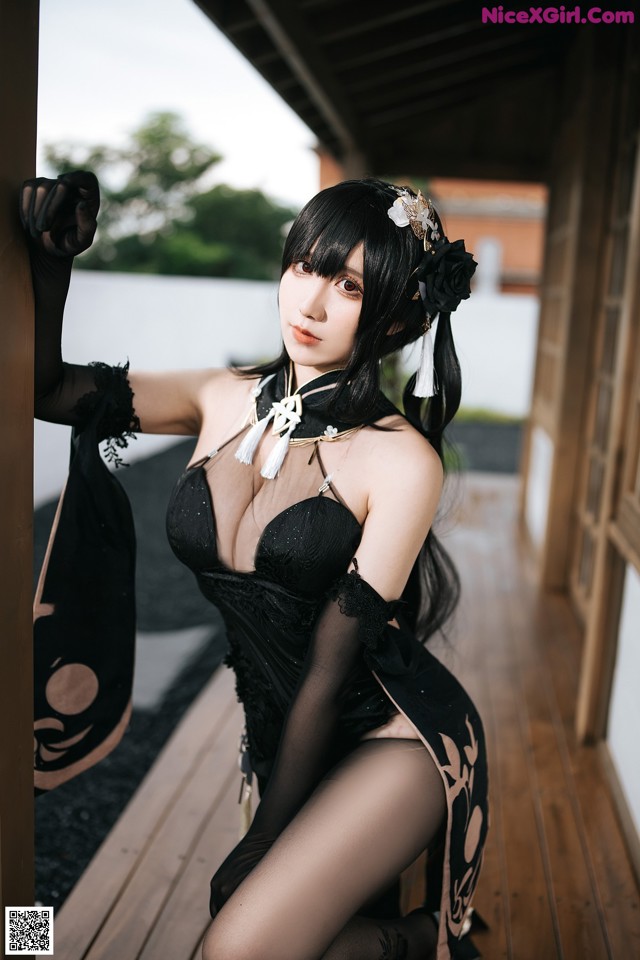A woman in a black dress sitting on a wooden floor.