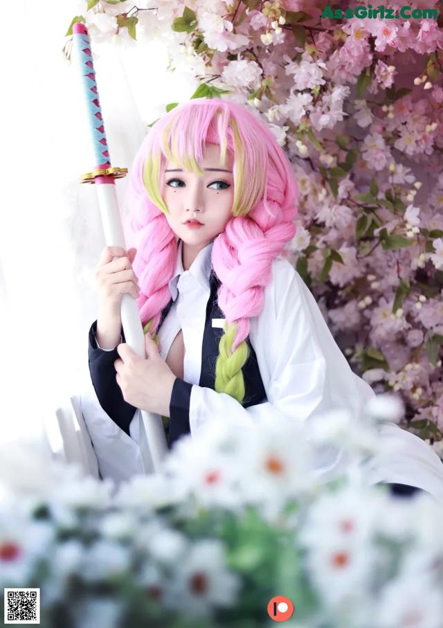 A woman with pink hair holding a sword in front of flowers.